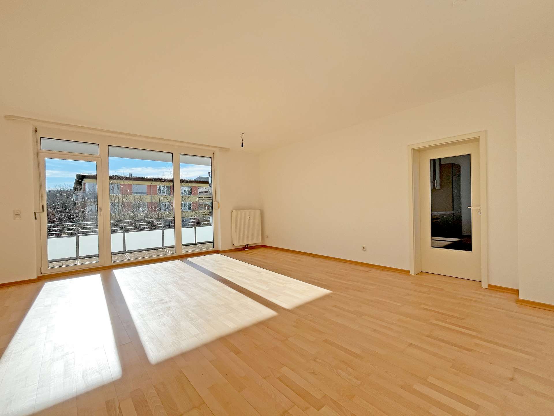 Wohnzimmer mit hellem Parkettboden und Balkonzugang